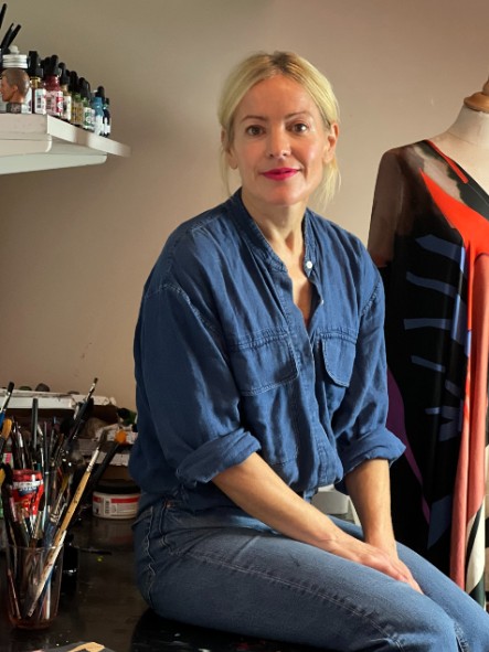 Stina Persson sitter p sitt arbetsbord bland penslar och frger.